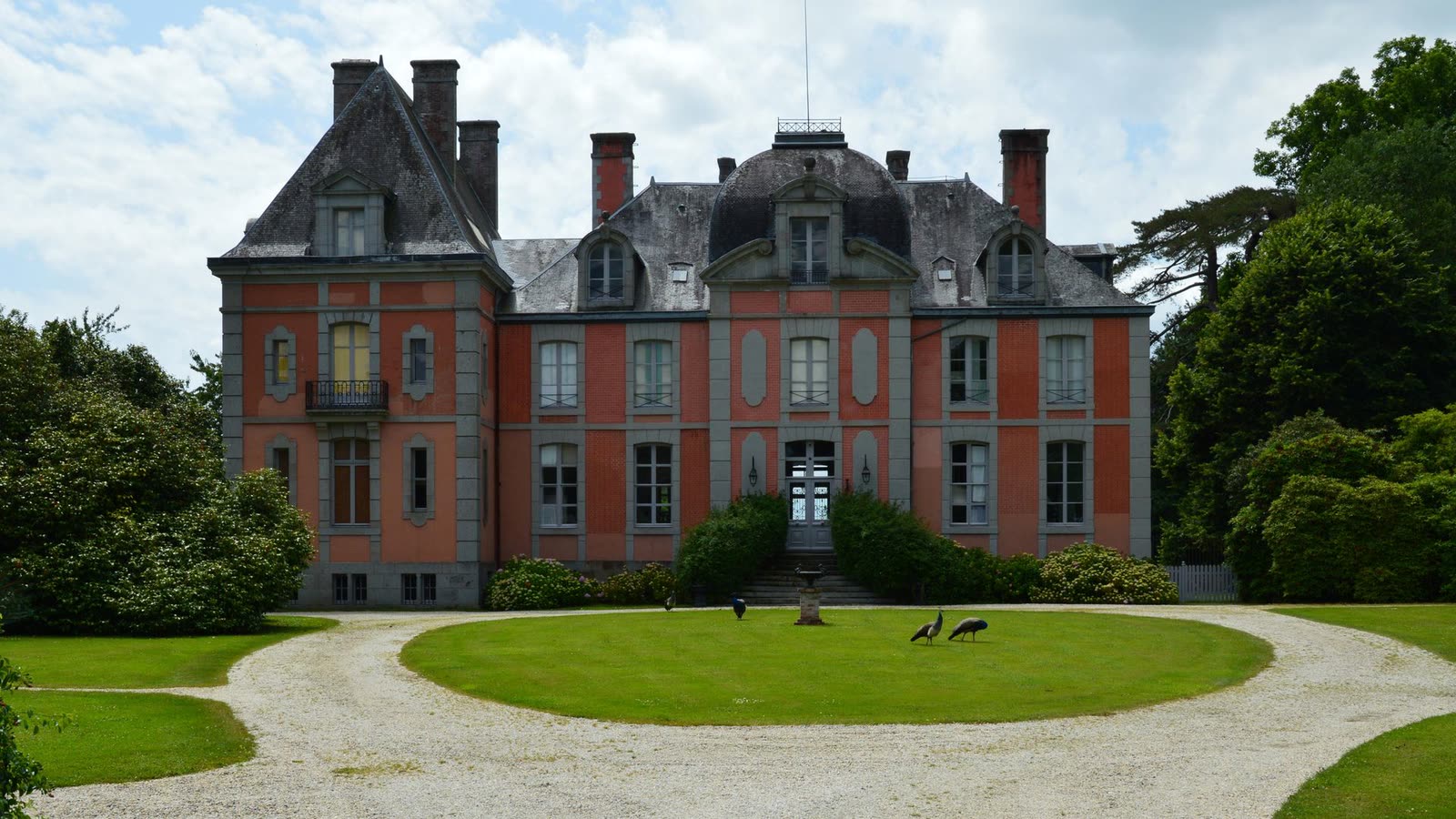 Château en brique rouge à toiture d’ardoise, devant une allée circulaire